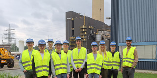 Studenten auf dem Kraftwerksgelände. Kraftwerksgebäude und Rauchgaskamin im Hintergrund.