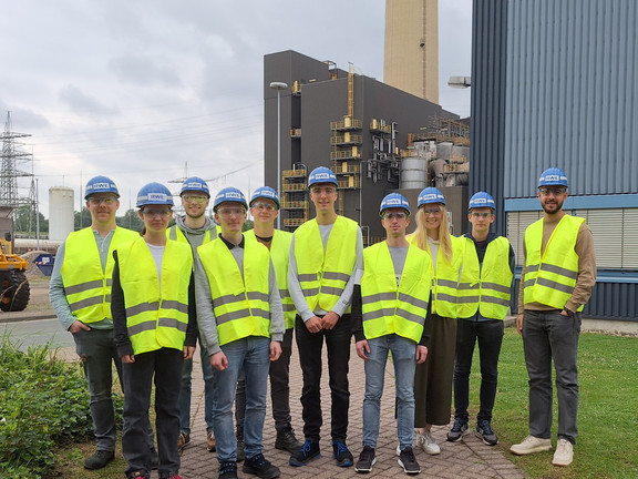 Studenten auf dem Kraftwerksgelände. Kraftwerksgebäude und Rauchgaskamin im Hintergrund.