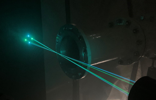 In the figure, the beam pairs (blue/green) of the LDA can be seen in front of the opened pipe end. The blue beams are arranged vertically, the green beams horizontally. At the cross point of all beams, the measuring volume is located in the very center in front of the pipeline